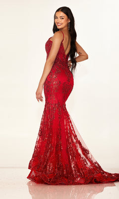 A woman in the Long Prom Dress: Cecilia Couture 2641, a fitted floor-length red mermaid gown with sequin accents and a sheer corset bodice, stands sideways and smiles over her shoulder against a plain light background.