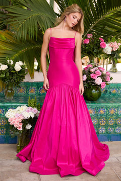 A woman wearing the Ava Presley 26422 drop-waist mermaid prom gown in bright pink stands before green foliage and floral arrangements, with a patterned tile wall behind her.