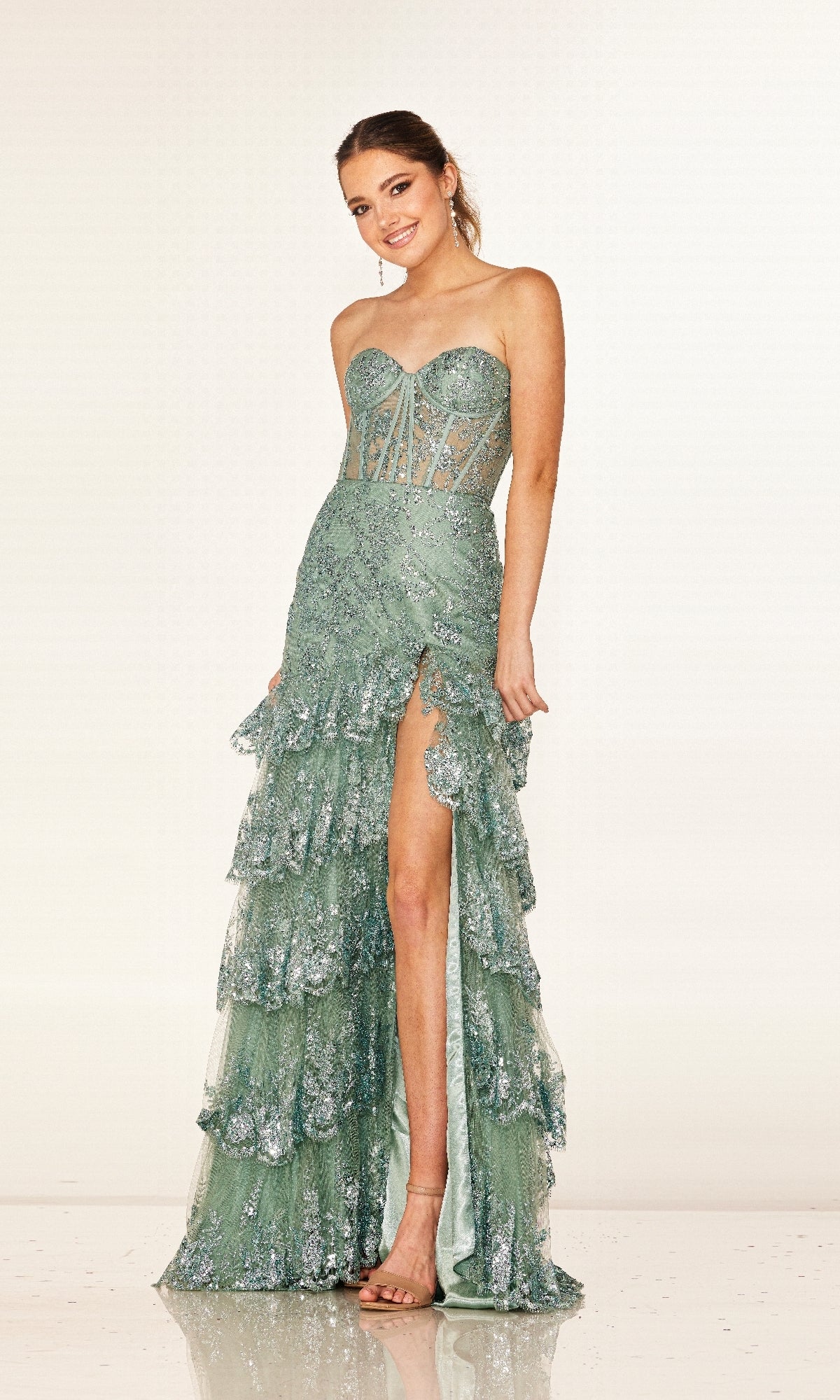 A woman wearing the Cecilia Couture 2642 long prom dress, featuring a strapless corset bodice, sequin accents, ruffled tiered skirt with a high slit, stands smiling against a plain background.