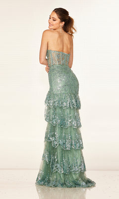 A woman models the Cecilia Couture 2642, a strapless green sequined long prom dress with a corset bodice and tiered layered skirt, standing against a plain light background and smiling over her shoulder.