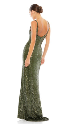A woman stands facing away from the camera against a white background, wearing the Mac Duggal 26443 Sexy Long Sequin Formal Dress—a fitted, backless, floor-length green gown—with her hair in a bun.