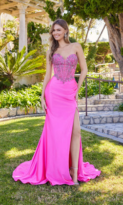 A woman stands outdoors in the Juliet JT2648K long prom dress, featuring a strapless embellished corset bodice, satin sheath skirt with a high slit, surrounded by greenery and stone steps.