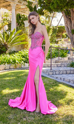 A woman stands outside in the Juliet JT2648K long prom dress, a fuchsia gown with a strapless embellished corset bodice, satin sheath skirt, and high slit, surrounded by greenery and stone structures.