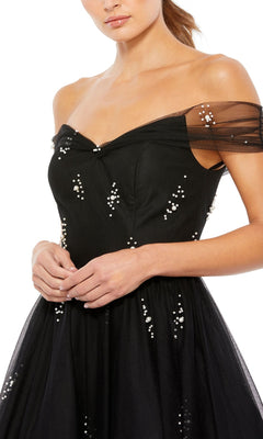A woman wears the Black Midi Wedding-Guest Dress: Mac Duggal 26498—an off-the-shoulder black midi dress with sheer sleeves and scattered white bead embellishments.