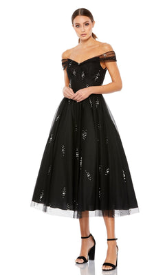 A woman wears the Mac Duggal 26498 black midi wedding-guest dress with off-the-shoulder neckline, sequin accents, and a flared skirt, styled with black high-heeled sandals.
