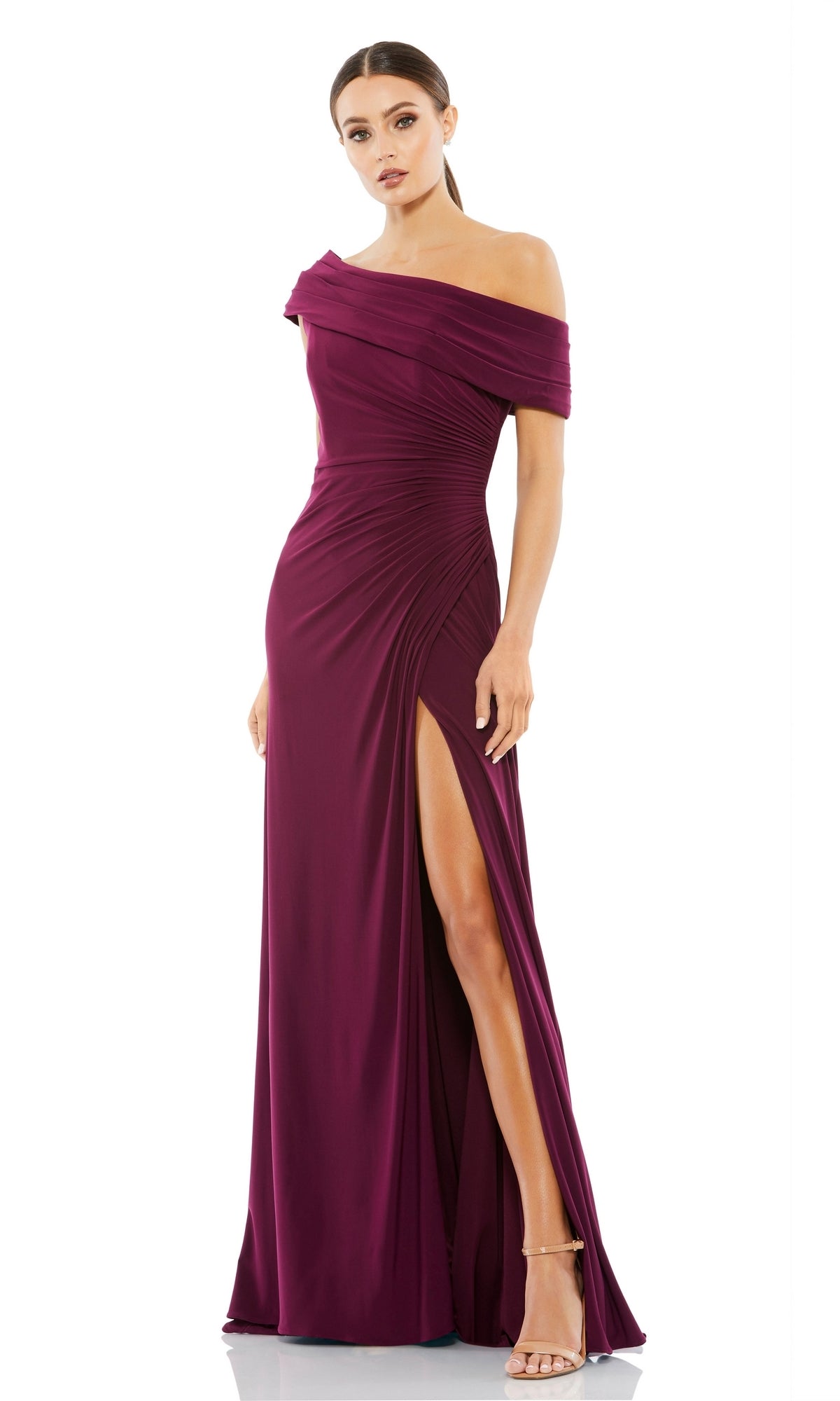 A woman in the Mac Duggal 26517 one-shoulder long prom dress with a thigh-high slit and strappy heels stands against a white background.