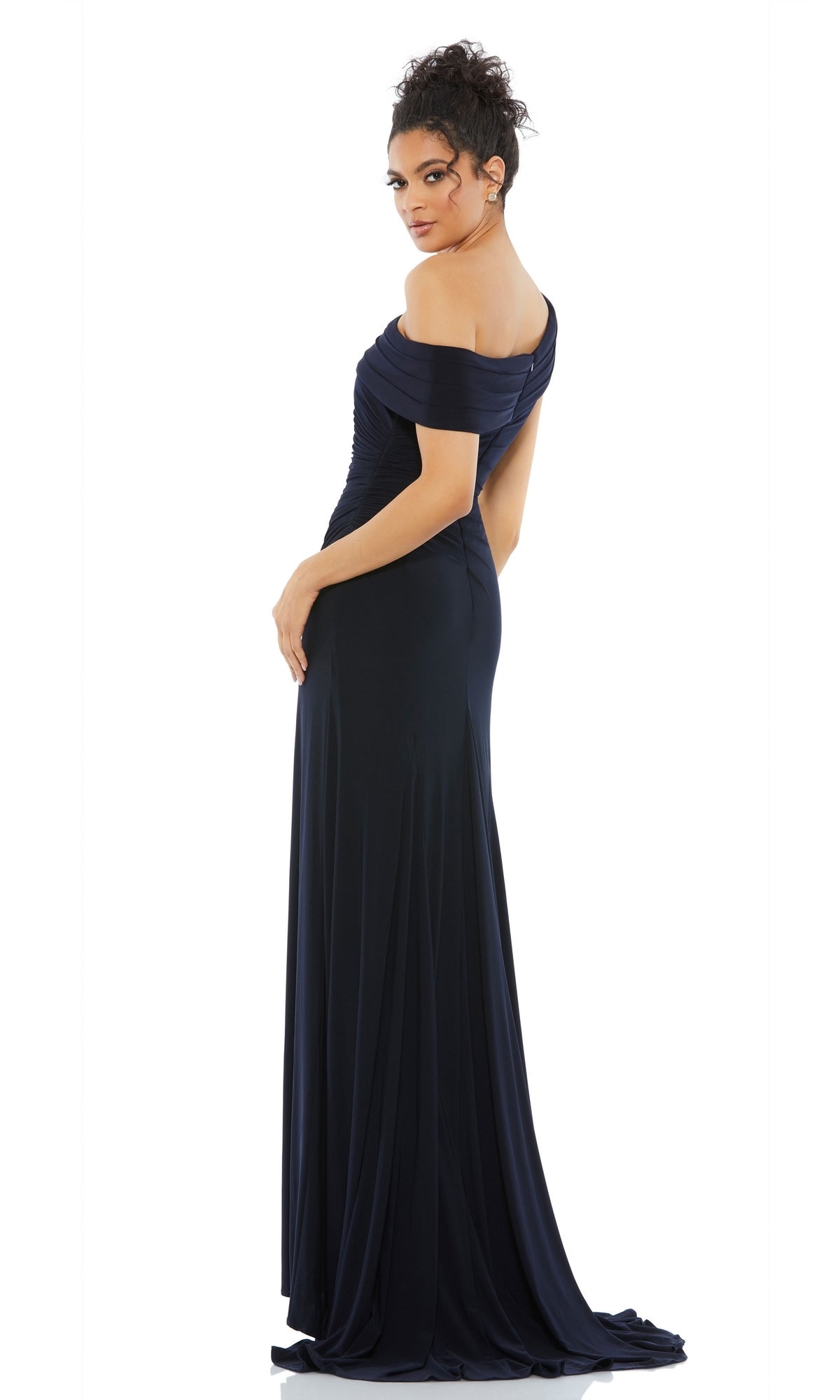 Woman in a navy blue Mac Duggal 26517 one-shoulder, floor-length prom dress stands with her back slightly turned, looking over her shoulder.