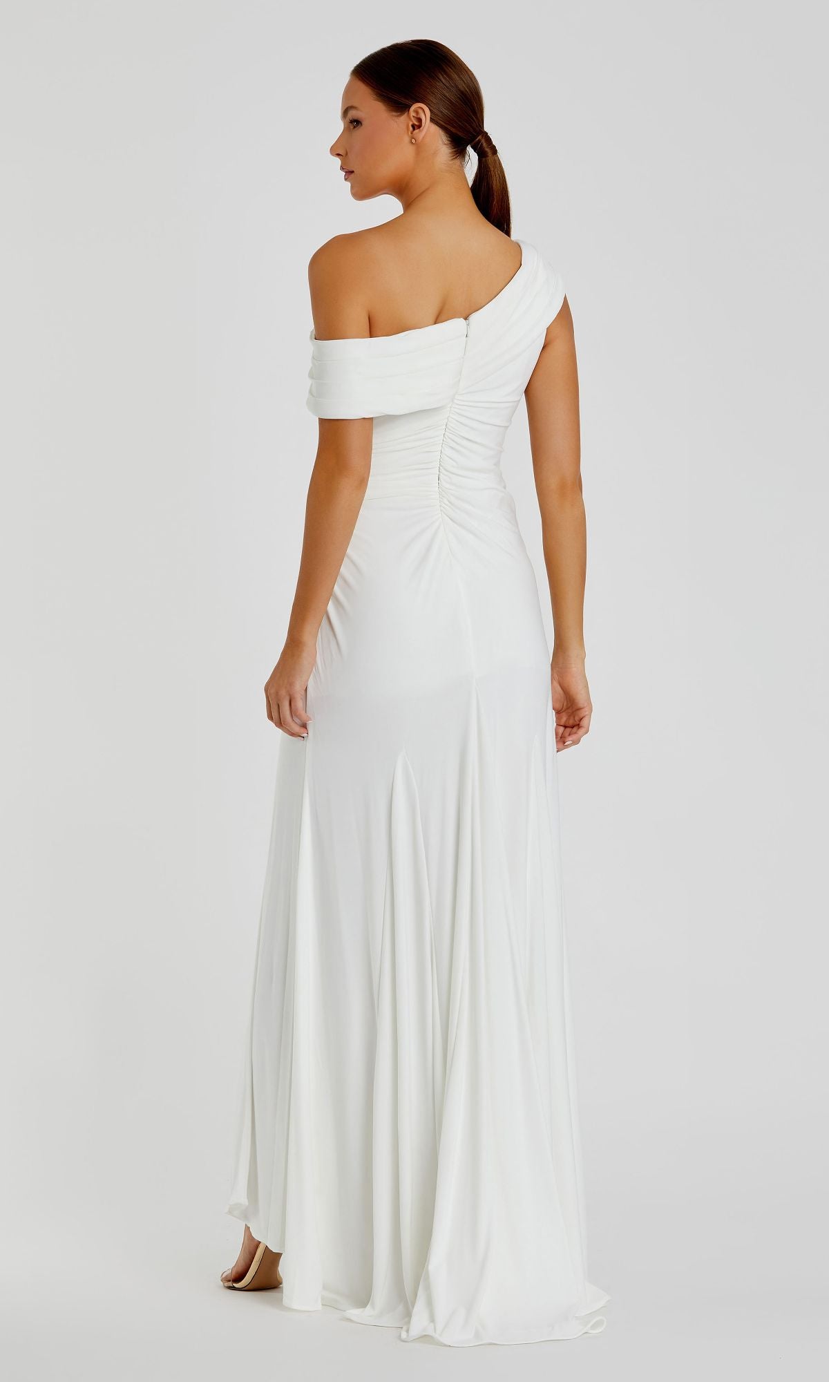 A woman faces away, wearing the Mac Duggal 26517 one-shoulder long prom dress with a fitted bodice and slight train.