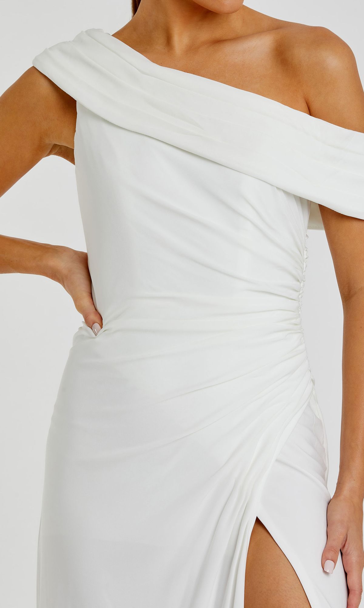 A woman stands confidently with one hand on her hip, wearing the Mac Duggal 26517 one-shoulder long prom dress featuring a ruched bodice and a thigh-high slit.