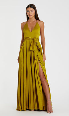 Woman wearing the Mac Duggal 26531 Bowed Long Halter Formal Dress, an olive-green pleated gown with a deep V-neckline, waist tie, and high leg slit, standing against a plain white background.