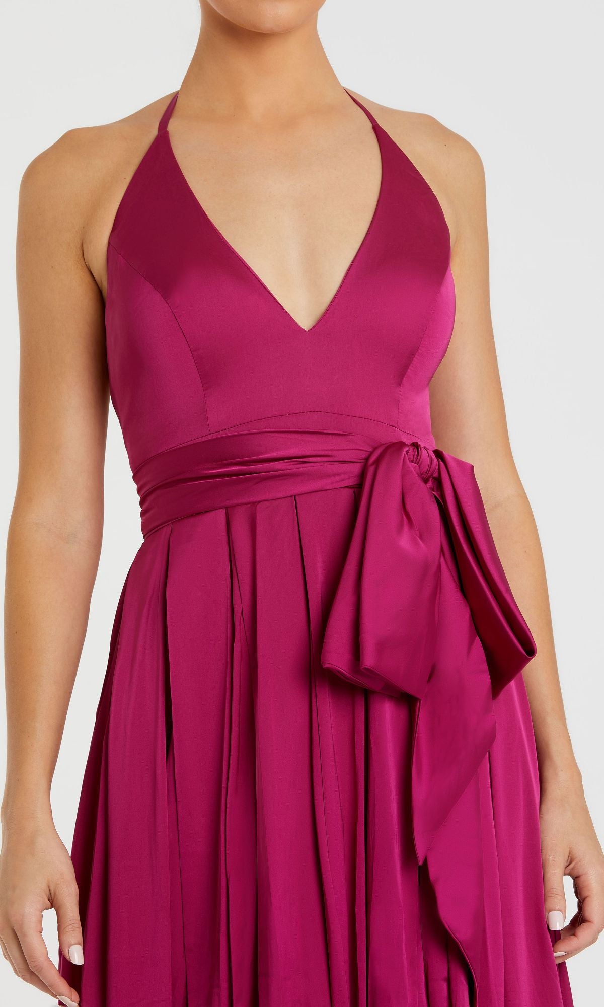 A person wearing the Mac Duggal 26531 Bowed Long Halter Formal Dress, featuring a sleeveless magenta design with a deep v-neck, wide waistband, side bow, and an elegant long a-line evening gown silhouette.