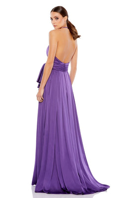 A woman in a floor-length, backless Bowed Long Halter Formal Dress (Mac Duggal 26531) stands facing away, her hair styled in a low ponytail.