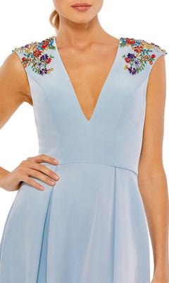 A woman wearing the Cap-Sleeve Long Formal Dress by Mac Duggal 26540, featuring a light blue deep V-neck design with colorful embroidered floral embellishments on the shoulders.