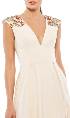 A woman wears the Cap-Sleeve Long Formal Dress: Mac Duggal 26540, a cream-colored A-line gown with a deep V-neck and colorful floral embroidery on the shoulders.