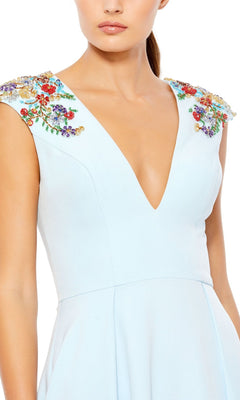 A woman wearing the Cap-Sleeve Long Formal Dress: Mac Duggal 26540, a light blue gown featuring a deep v-neck and colorful floral embellishments on the shoulders.