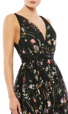 A woman wears the Mac Duggal 26557 Black Floral Wedding Guest Dress, a sleeveless black dress with a deep V-neck and multicolored floral embroidery—perfect for chic parties.