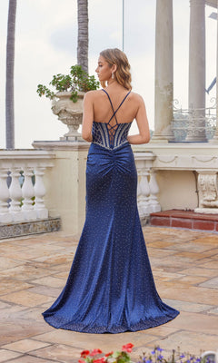 A woman stands outdoors facing away, wearing the Juliet JT2655S long prom dress—a floor-length, navy blue gown with strappy open back, ruched detailing, and glittering rhinestones.