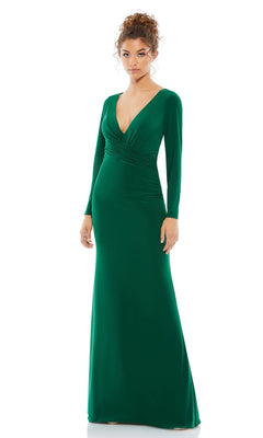 A woman stands against a white background wearing the Mac Duggal 26573 Long Sleeve Long Formal Dress—a floor-length green gown with a deep V-neckline and fitted waist.