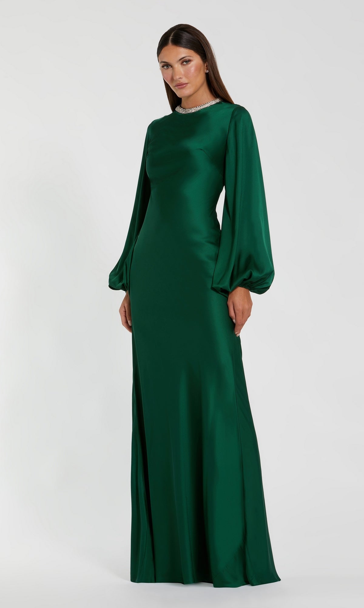 A woman stands against a plain white background wearing the Mac Duggal 26575, a long sleeve formal dress in emerald. Featuring a fitted bodice and slightly flared skirt, this modest evening gown radiates timeless elegance and sophistication.
