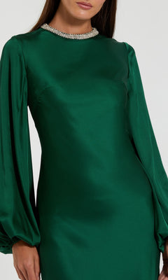 A woman models the Mac Duggal 26575 Long Sleeve Long Formal Dress, featuring emerald green satin, a beaded neckline, and modest full-length sleeves—an elegant evening gown showcased from shoulders to thighs against a plain background.