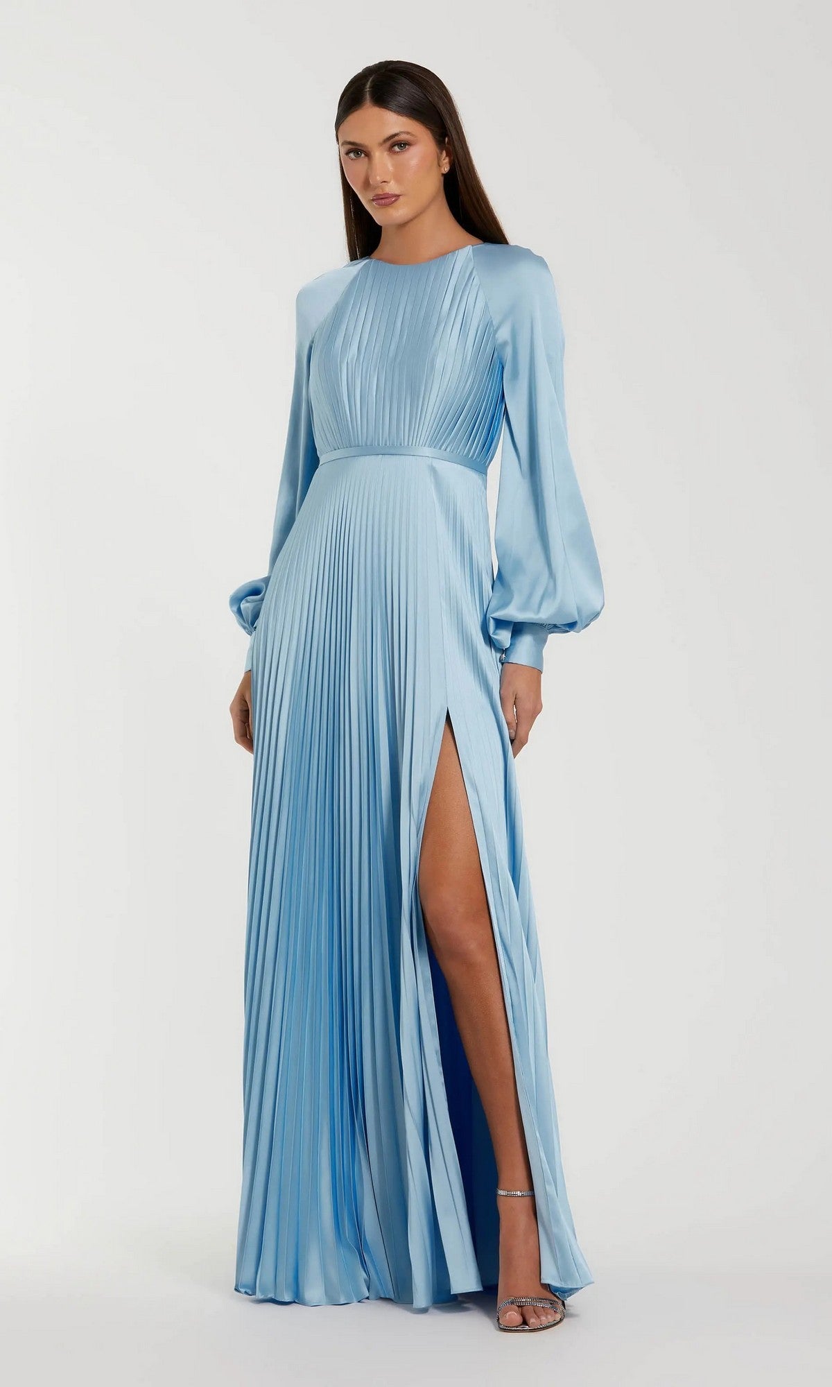 A woman poses elegantly against a white background wearing the Mac Duggal 26590, a light blue long formal dress featuring pleats, long sleeves, and a high slit.