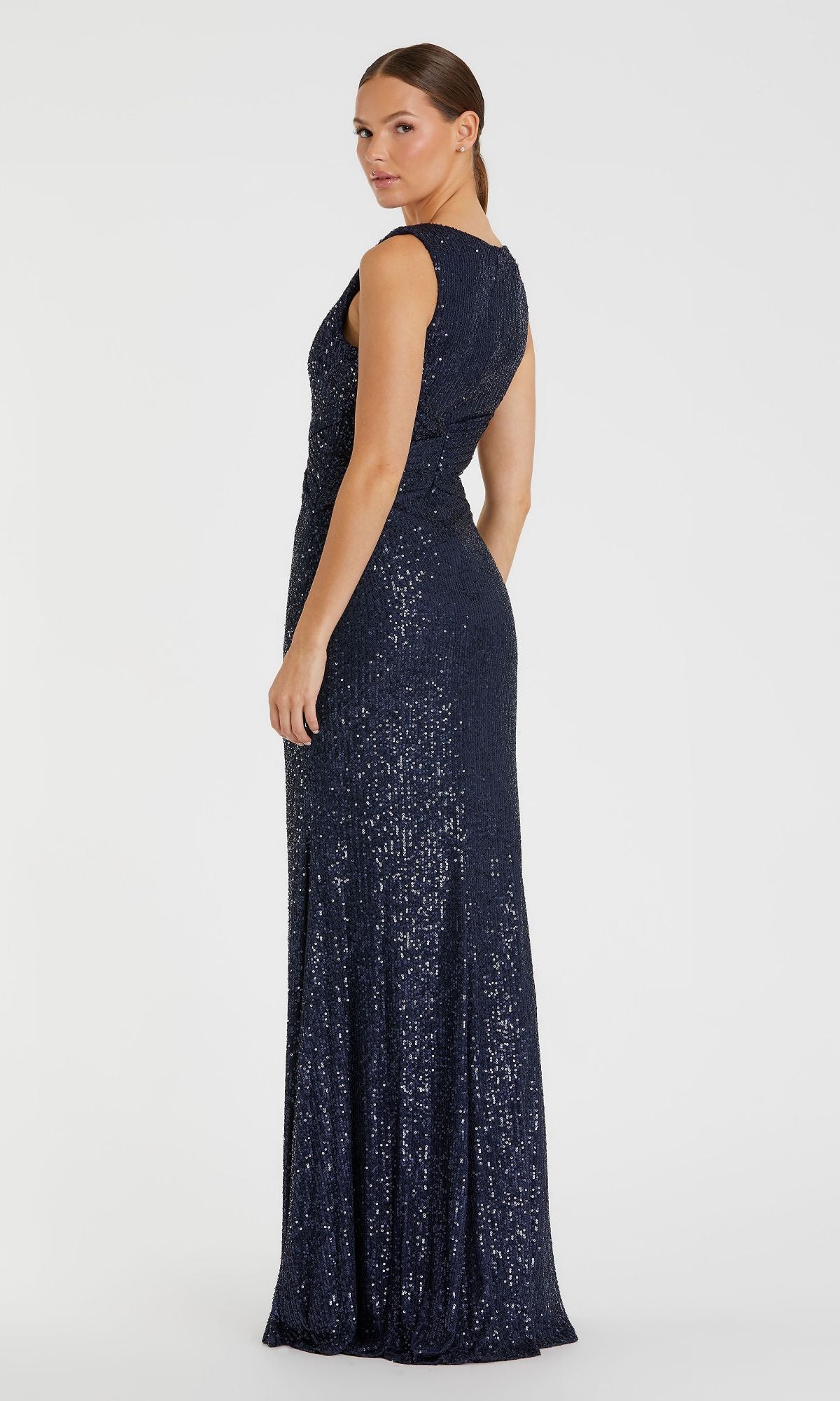 A woman stands sideways against a plain white background wearing the Mac Duggal 26598, a dark blue, sleeveless long formal dress adorned with sequins.