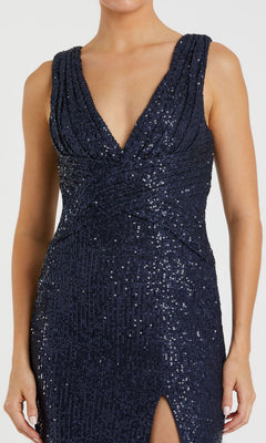 A woman wears the Mac Duggal 26598 sleeveless long formal dress in navy blue, featuring sequins, a deep V-neckline, and a high slit—an elegant evening or prom gown.