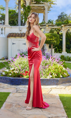 A woman in the Juliet JT2659S long prom dress with a thigh-high slit stands on a stone path by a circular flower bed and white columns in a garden.