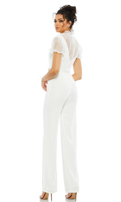 A woman faces away, wearing the Long Formal Jumpsuit 26621 by Mac Duggal, featuring a white high neck, short sheer sleeves, a belted waist, and high heels against a plain background.
