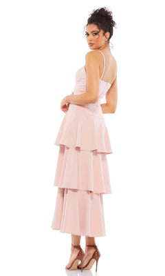 A woman stands looking over her shoulder in the Short Wedding Guest Dress 26629 by Mac Duggal—light pink, tea length with ruffle layers and thin straps—paired with nude high heels.