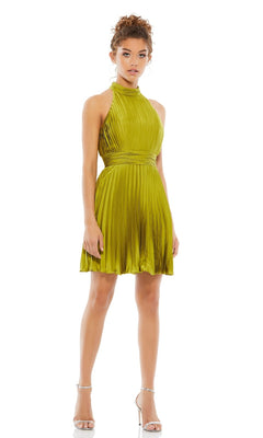 A woman models the Mac Duggal 26645 short pleated hoco dress in lime green, featuring a high neckline and fitted waist, paired with silver heels against a plain white background.