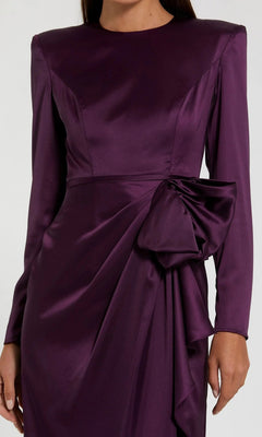 A person in the Mac Duggal 26676 Bold-Shoulder Long Formal Dress, crafted from dark purple satin with strong shoulders and a large waist bow—an elegant evening gown ideal for special occasions.