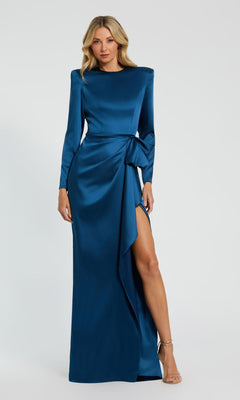 A woman stands against a plain light background wearing the Mac Duggal 26676 Bold-Shoulder Long Formal Dress—a bra-friendly, teal satin evening gown with long sleeves, a high slit, and side bow detail.