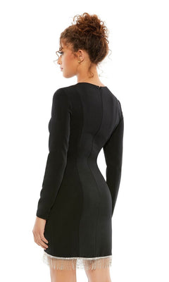 A woman with curly hair in a bun wears the Short Homecoming Dress 26679 by Mac Duggal—a fitted black party dress with long sleeves and a beaded fringe hem—standing with her back to the camera against a white background.