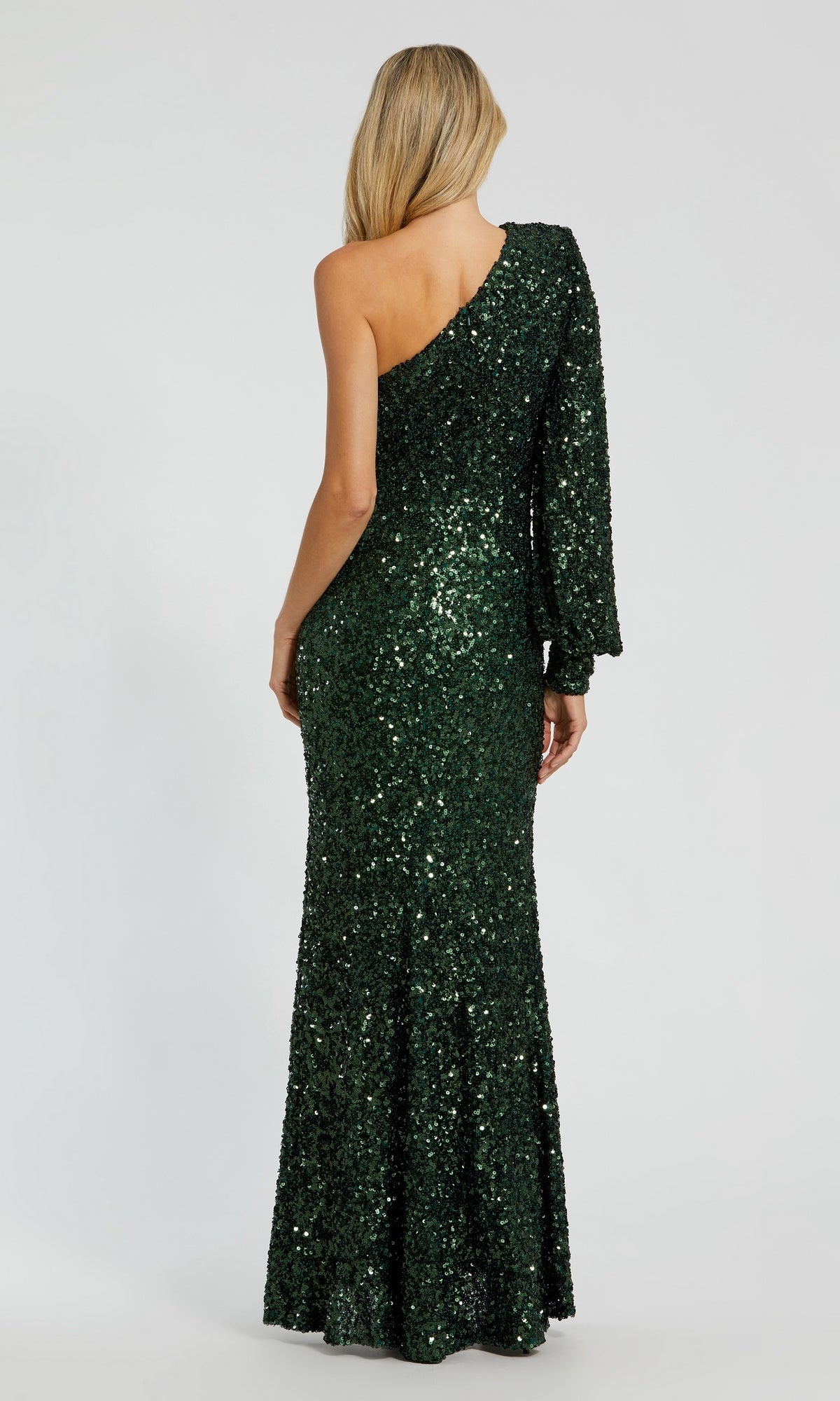 A person wearing the Mac Duggal 26717 One-Sleeve Sequin Formal Gown in dark green stands facing away against a plain light background. This floor-length gown shimmers with sequins, making it the perfect sparkly choice for special occasions.