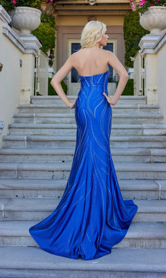 A woman in the Juliet JT2673R long prom dress stands on outdoor steps, her strapless, royal blue, floor-length gown flowing elegantly as she faces away from the camera.