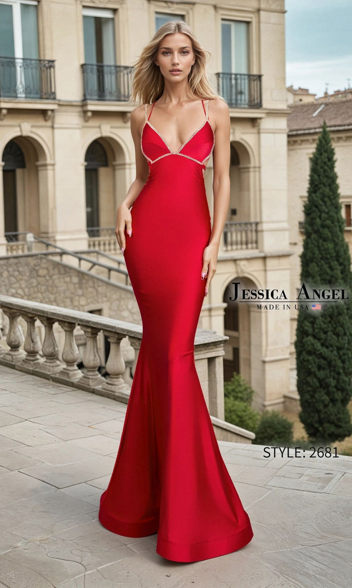A woman stands on a stone terrace in front of a grand building wearing the Long Prom Dress: Jessica Angel 2681 in red—a fitted, floor-length mermaid gown with thin straps and a satin finish.