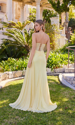 A woman wearing the Long Prom Dress: Juliet JT2684A, featuring a strapless design and lace-up back, stands on grass near stone steps and greenery, facing away from the camera.