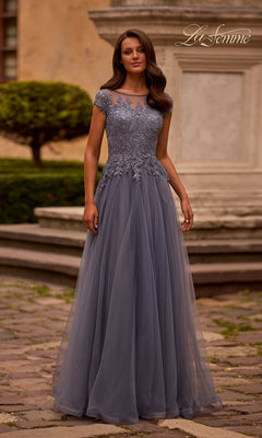 A woman stands outdoors near stone steps and greenery, wearing the La Femme 26893 long formal dress in smoky blue, featuring short sleeves, a lace embroidered bodice, and a flowing tulle skirt.
