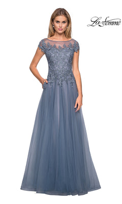 A woman stands wearing the Long Formal Dress: La Femme 26893, a floor-length blue gown with a lace embroidered bodice and short sleeves. Perfect as a mother of the bride dress, it features a sheer neckline and a flowing tulle skirt. The “La Femme” logo appears in the corner.