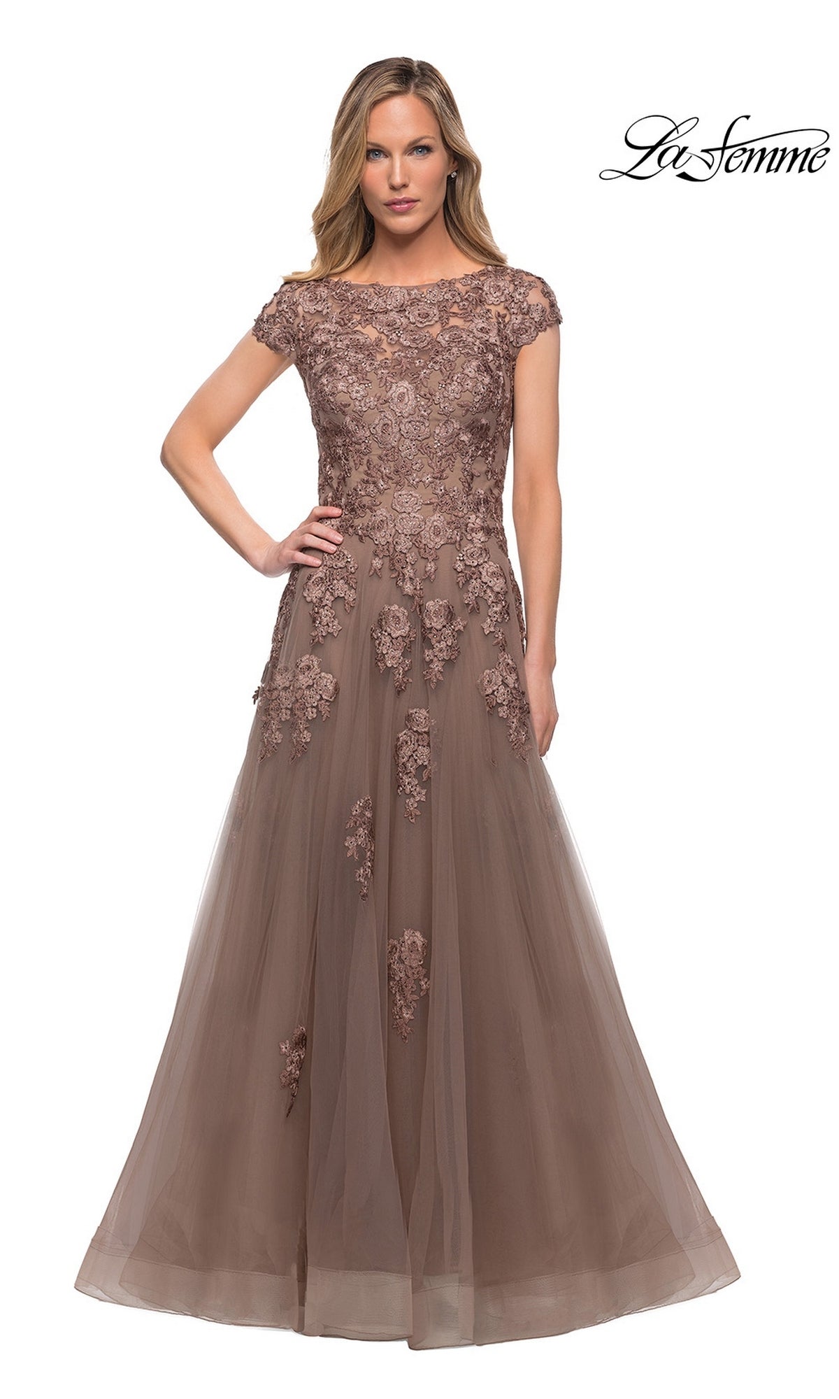A woman wearing the La Femme 26907 long formal dress in cocoa, featuring a floor-length A-line silhouette with short sleeves and embellished lace appliques on the bodice and skirt, stands against a plain white background.