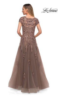A woman stands with her back to the camera against a white background, wearing the Long Formal Dress: La Femme 26907—a floor-length brown gown featuring floral embroidery and embellished lace appliques. The “La Femme” logo is displayed in the top right corner.