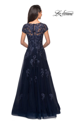 A woman wearing the La Femme 26907 long formal dress, a floor-length navy blue gown featuring embellished lace appliques and a sheer lace back, stands facing away.