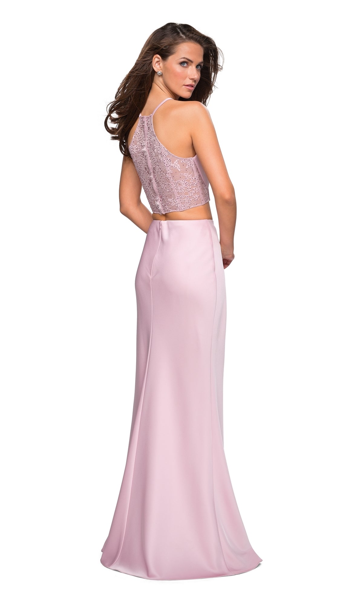 A woman stands against a white background, looking back over her shoulder in the La Femme Two-Piece Blush Pink Satin Prom Dress 26926, featuring a sleeveless lace crop top with a sheer back and a floor-length satin skirt.