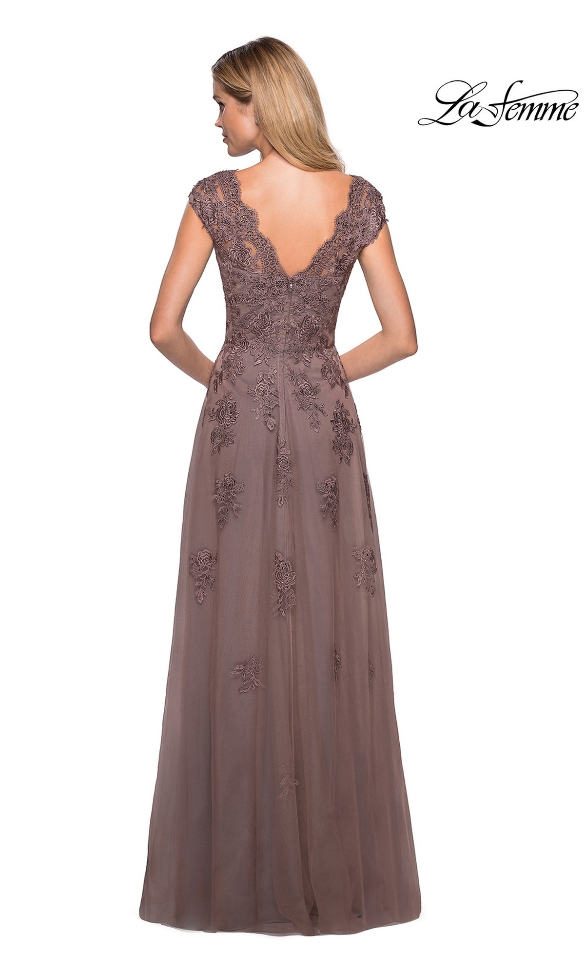 A woman in the La Femme 26942 long formal dress, featuring mauve floral lace with delicate detailing and a deep V-back, stands against a white background—an elegant choice for a mother-of-the-bride gown.
