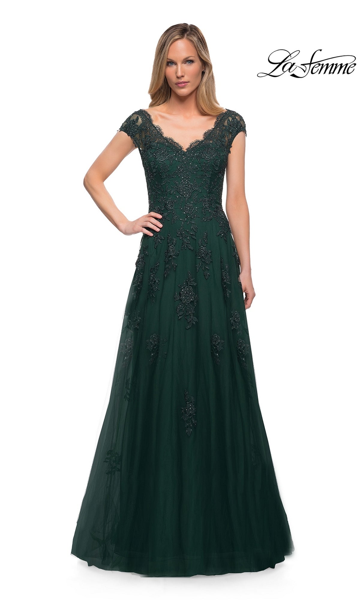 A woman wears the La Femme 26942 long formal dress in Dark Emerald, featuring cap sleeves, floor-length design, and lace with sequin embellishments. She stands against a white background with the La Femme logo in the top right corner.