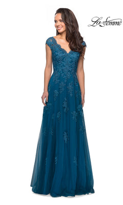 A woman is standing and smiling in the Long Formal Dress: La Femme 26942, a teal floor-length gown featuring lace floral detailing, cap sleeves, and a V-neckline. The La Femme logo appears in the top right corner.