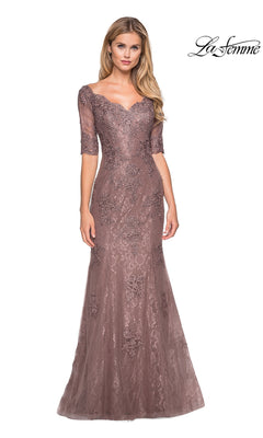 A woman models the “La Femme 26943” long formal dress in cocoa—a modest, floor-length gown with half sleeves, a fitted silhouette, exquisite floral embroidery and lace, sparkling rhinestone accents, and a flattering sweetheart neckline. Elegantly designed for special occasions such as mother-of-the-bride events. “La Femme” logo appears in the top right.