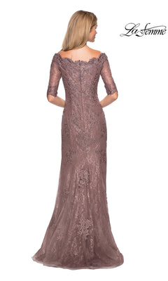 A woman stands with her back to the camera, wearing the La Femme 26943—a long mauve lace evening gown with half sleeves and an off-the-shoulder neckline. Rhinestone accents add elegant detail, making this modest formal dress a perfect choice for mothers of the bride. The “La Femme” logo is displayed in the upper right corner.