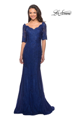 A woman poses against a white background, smiling in the La Femme 26943 long formal dress. This floor-length gown in marine blue features delicate lace, short sleeves, and a flattering sweetheart neckline. Rhinestone accents enhance the elegant and modest design, making it perfect for any special occasion. The “La Femme” logo appears in the top right corner.